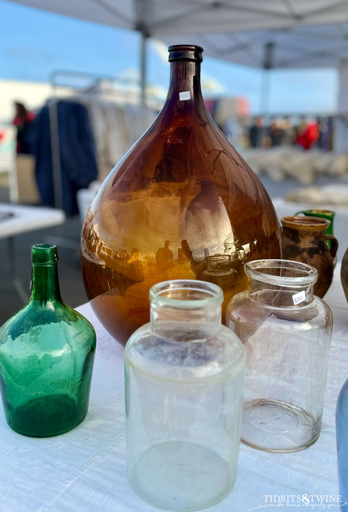 Assorted vintage glass bottles and large demijohns in green, amber, and clear hues.