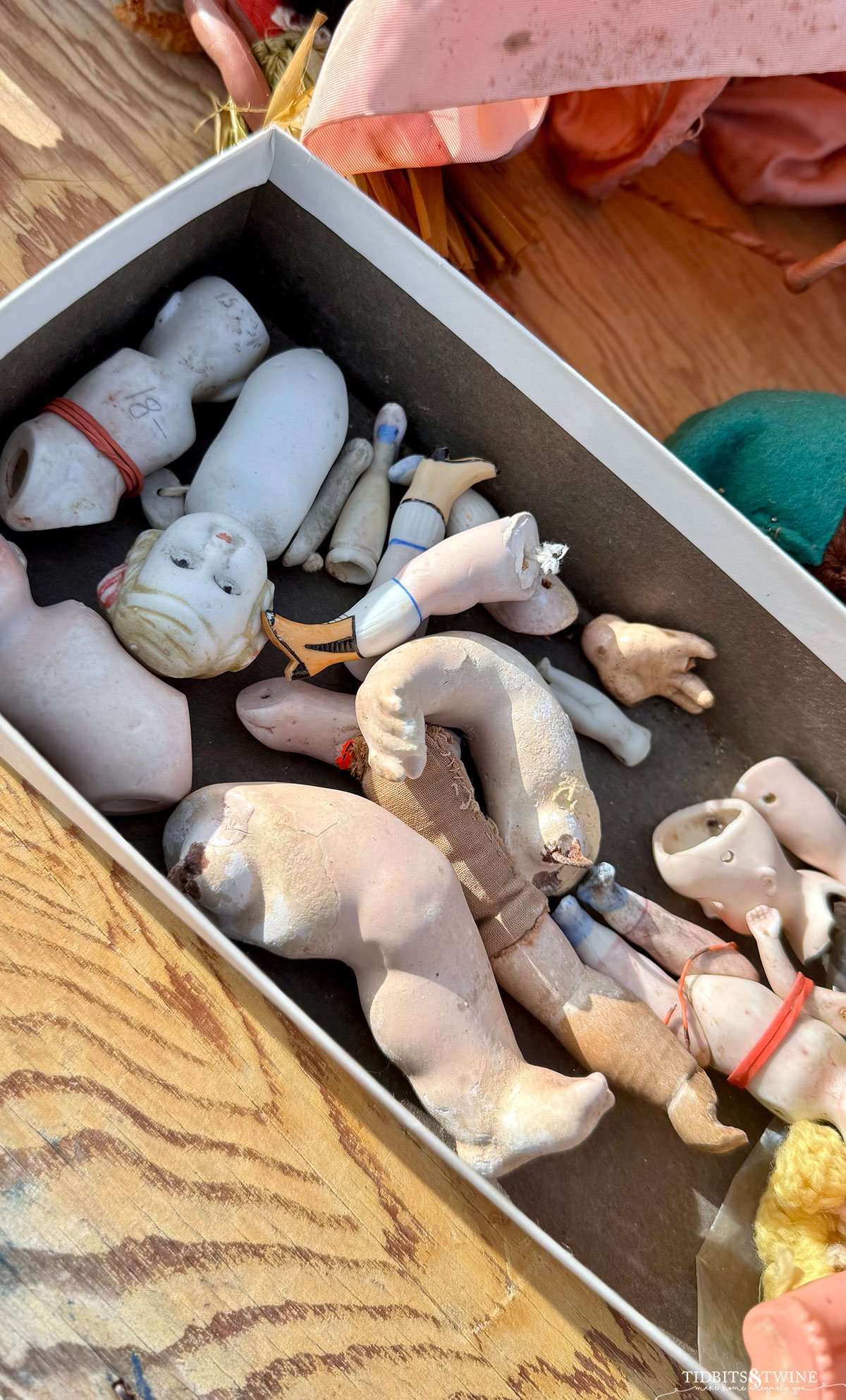 Vintage box filled with old doll parts, including a single tiny Frozen Charlotte partially hidden in the corner.