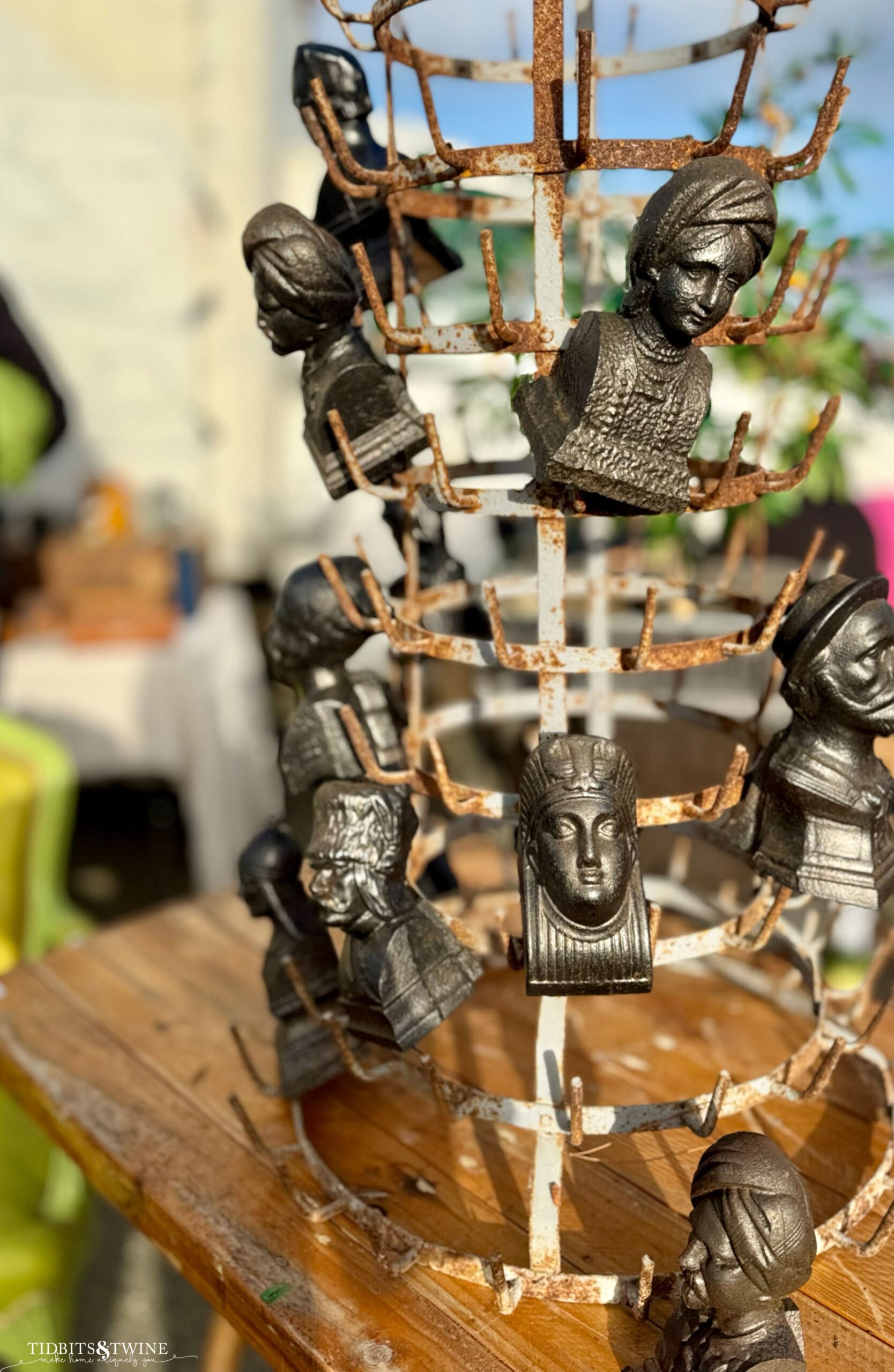 Rusty metal bottle drying rack with small cast busts clipped onto the spokes.