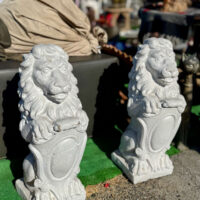 Two large white cement lion statues sitting side by side on concrete at the Alameda Antique Fair.