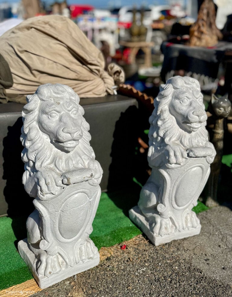 Two large white cement lion statues sitting side by side on concrete at the Alameda Antique Fair.