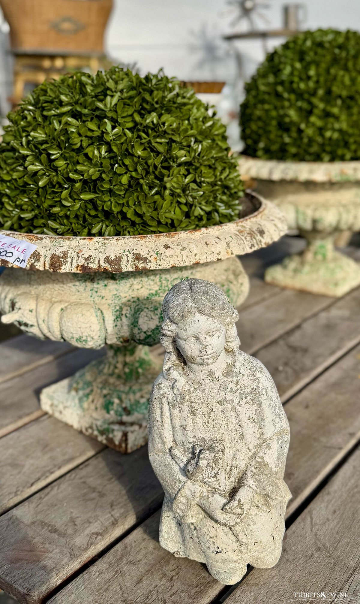 Weathered cement urns next to a statue of a child holding a bunny at an outdoor antique market.