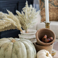 Fall coffee table vignette with five visual groupings&mdash;two pumpkins, pampas grass, stacked terra cotta pots, and a brass candlestick&mdash;demonstrating the rule of odds interior design