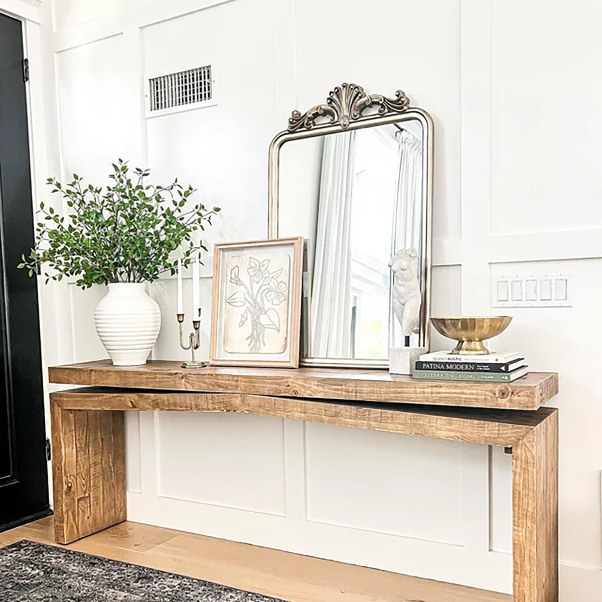 Warm entryway console with wood table, brass mirror, and greenery showing how to make your home look expensive using simple styling tricks.