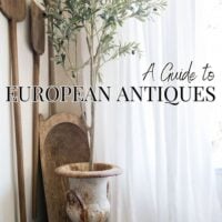 A European-style corner with antique bread paddles and a weathered urn holding an olive tree beside soft white curtains — a guide to European antiques and how to decorate with them.