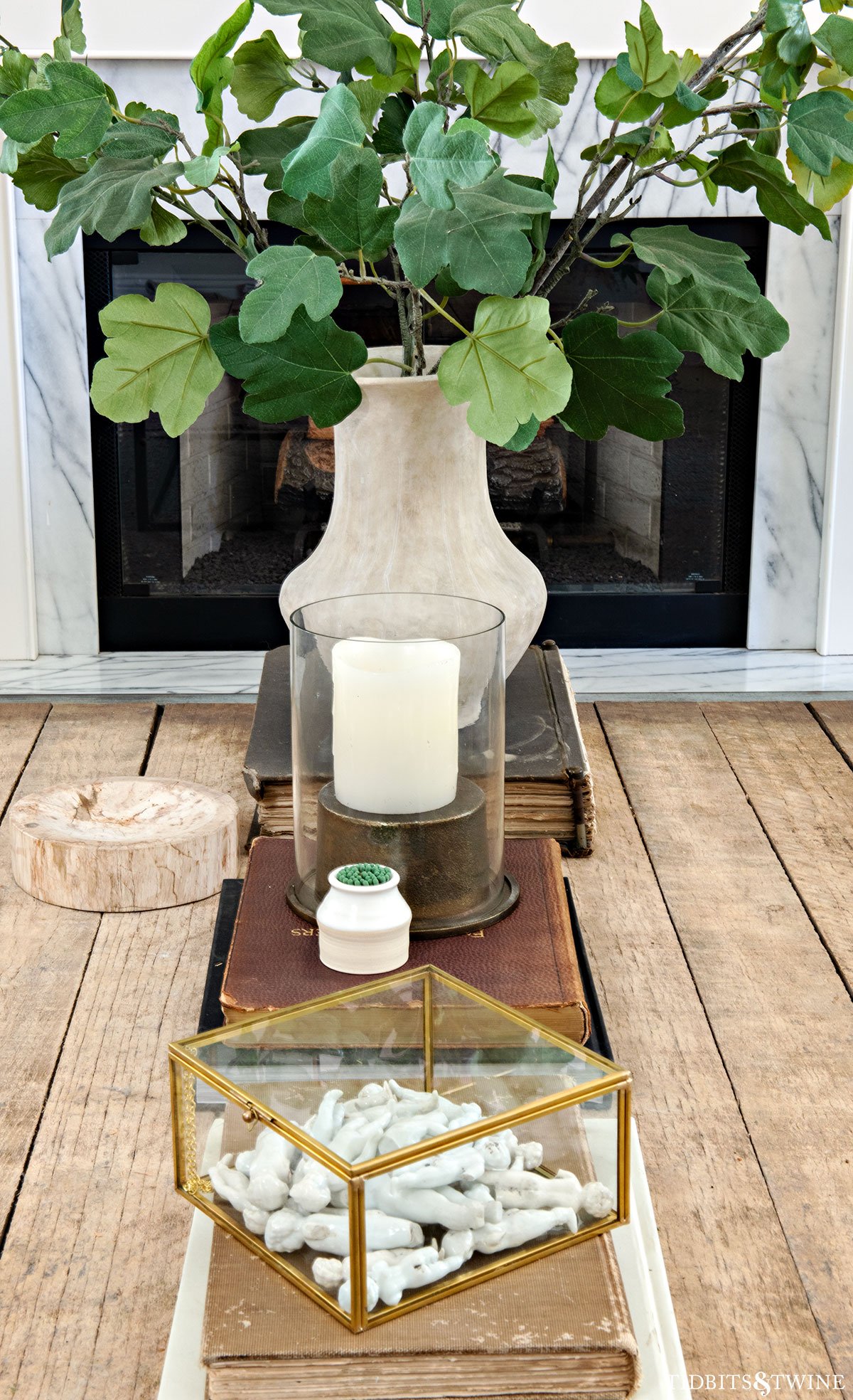 Coffee table styled with stacked books, glass box, and a tall vase of greenery to create height and layered dimension