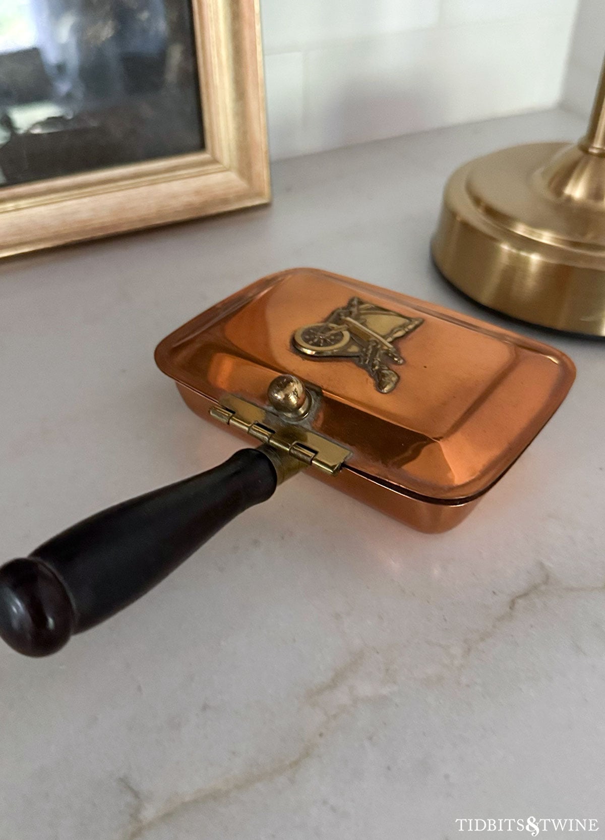 Early copper hinged silent butler with wooden handle, photographed on a kitchen counter.