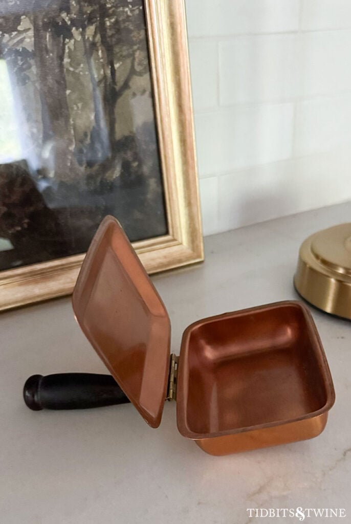 Open copper hinged silent butler showing shallow crumb pan and simple interior.