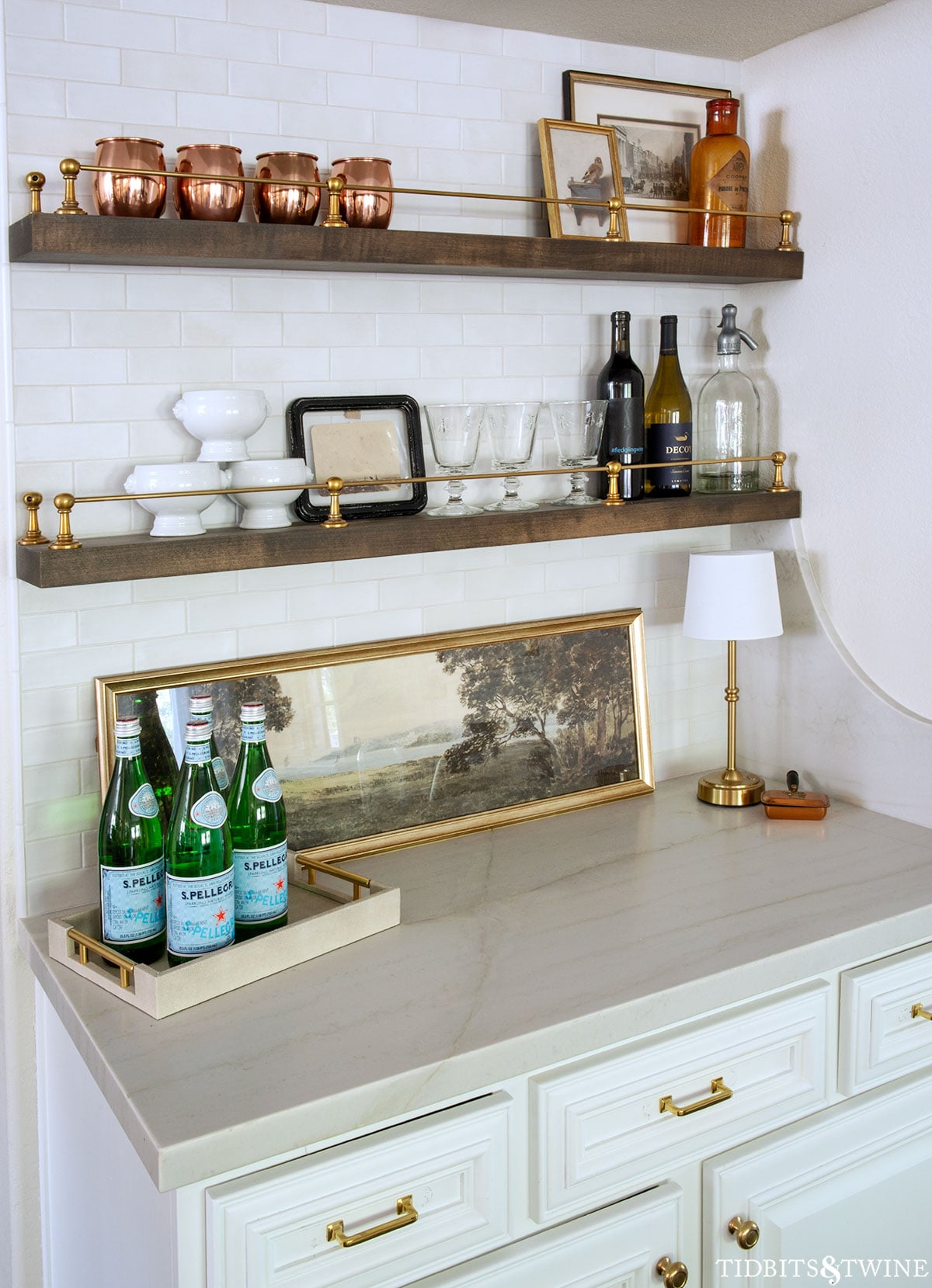 Copper silent butler resting on a bar counter beneath open shelves and vintage glassware.