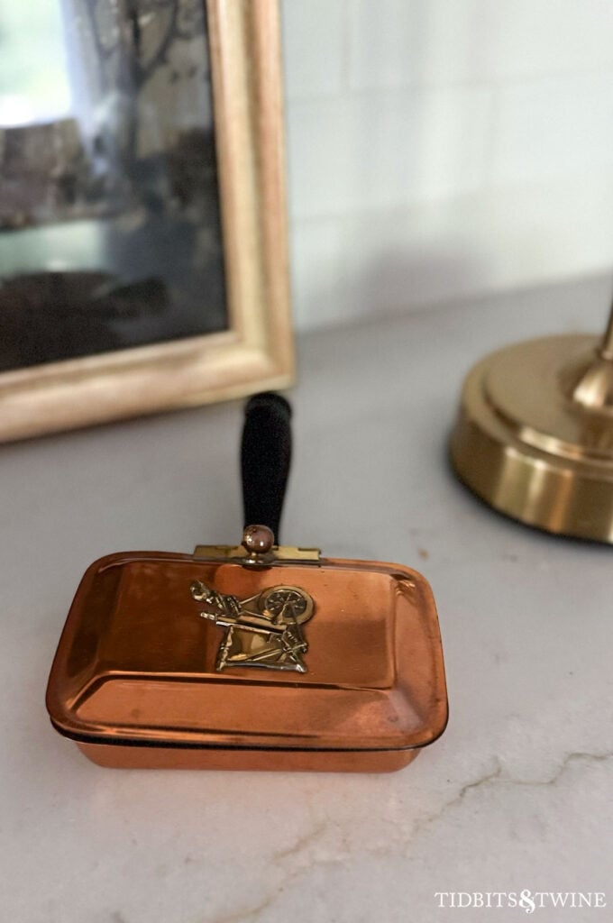 Antique copper hinged silent butler with carved wooden handle and decorative metal detail on the lid.