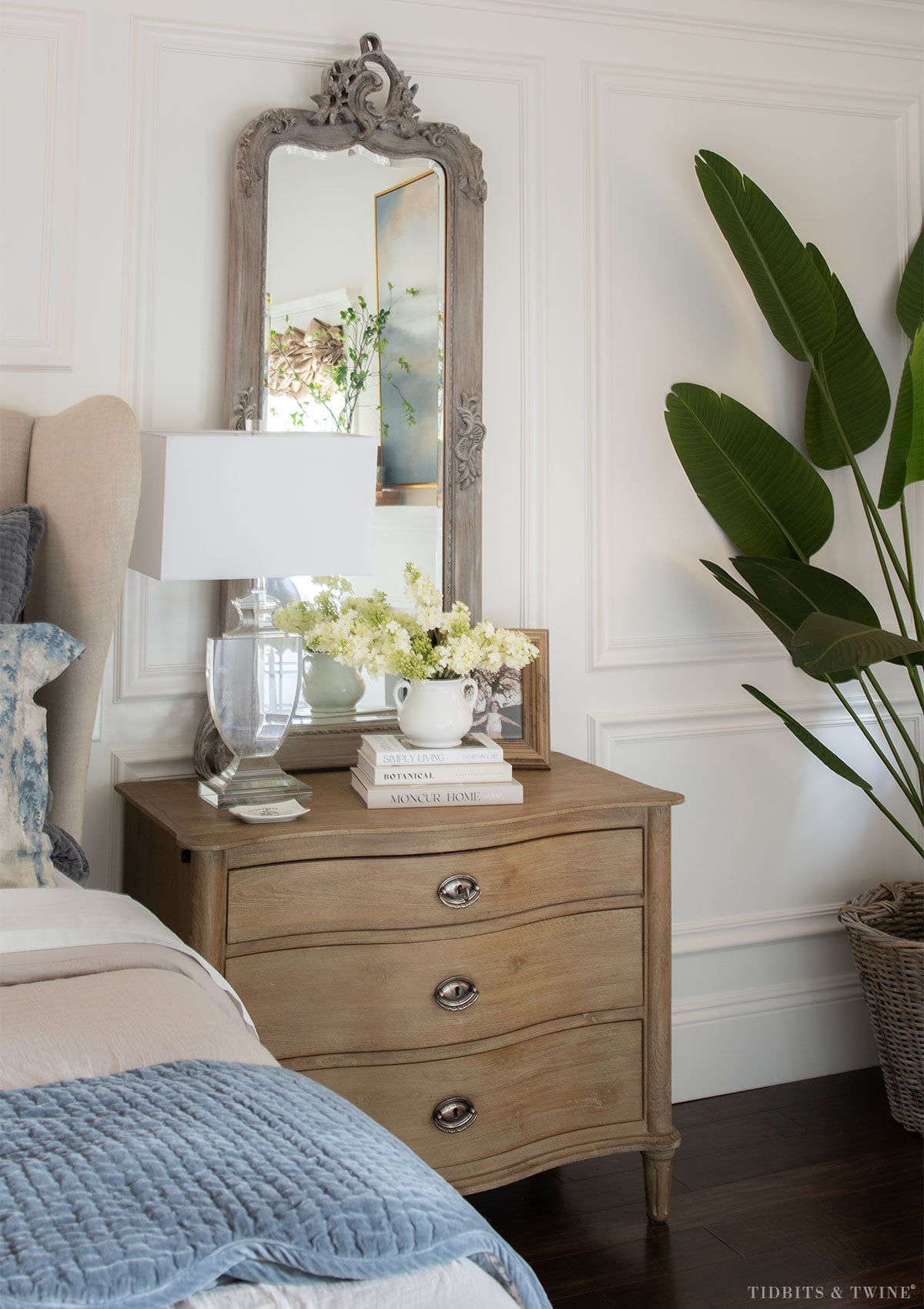 French-inspired nightstand decorating with mirror, lamp, stacked books, flowers and a personal photo