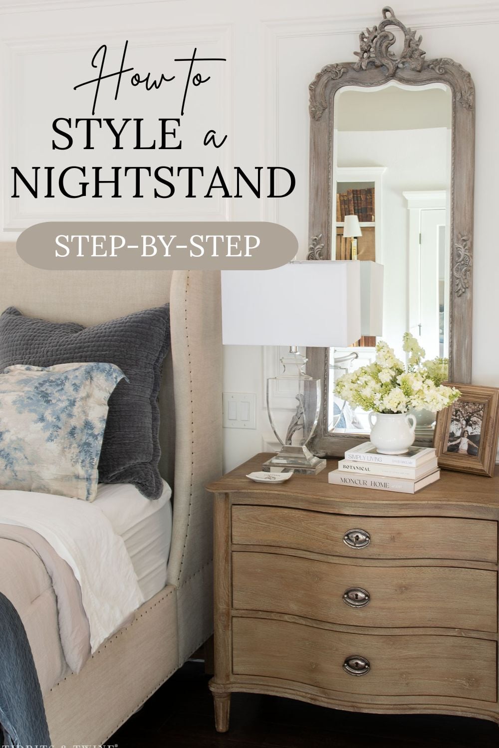 Nightstand decorating example with wood nightstand, mirror, lamp, stacked books, and flowers