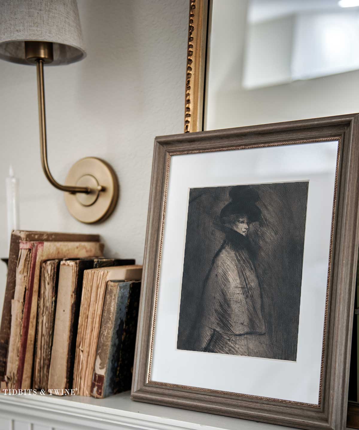 Framed moody portrait displayed on a living room mantel beside antique books and a brass wall sconce