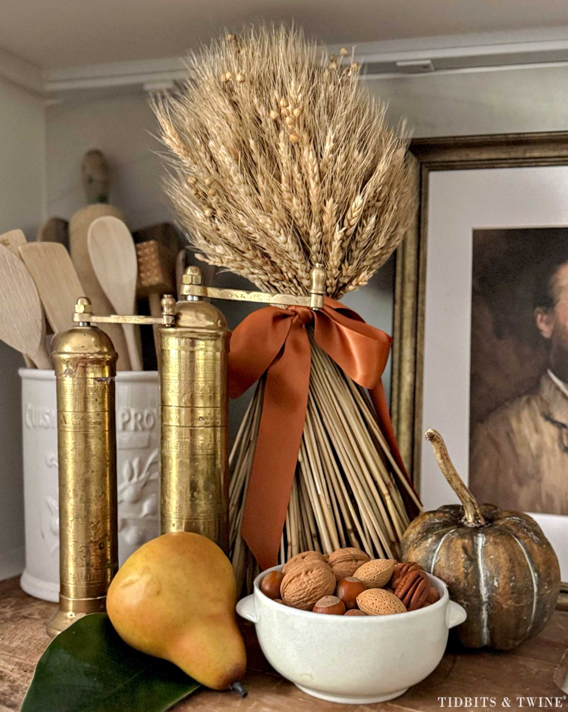 Fall kitchen vignette with wheat, antique brass mills, pear, nuts and a small pumpkin