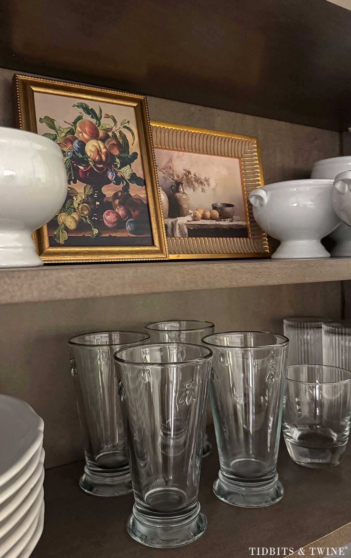 Small framed fall still life artwork tucked among white dishes and glassware